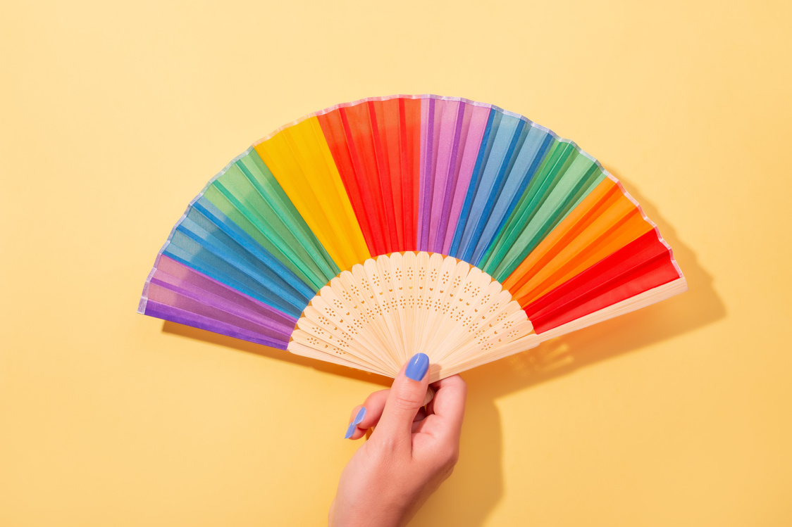 Hand with Manicure Holding Colored Fan on Yellow Background